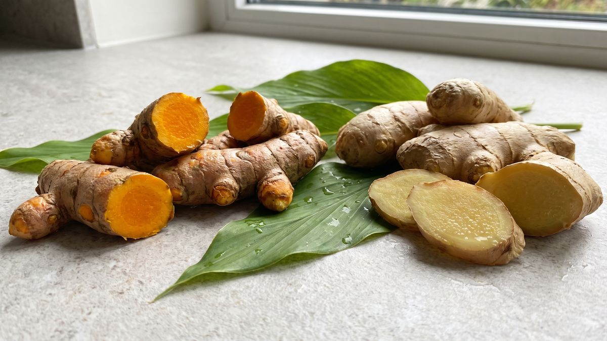 Fresh turmeric and ginger roots split open to show bright yellow and pale gold flesh